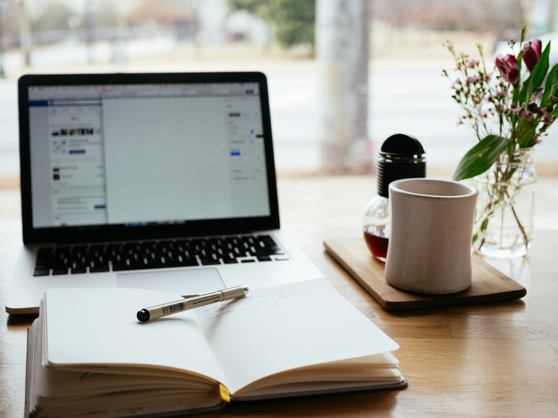 Calm workspace with an open notebook, pen, laptop, and natural light